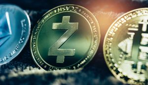 Drei physische Münzen, die Kryptowährungen repräsentieren - Ethereum, Zcash und Bitcoin - werden Seite an Seite auf einer dunklen, strukturierten Oberfläche angezeigt, wobei die Zcash-Münze besonders hervorsticht.