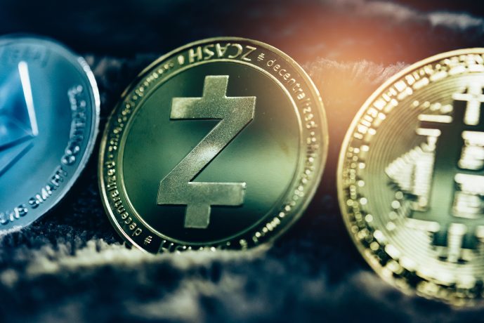 Drei physische Münzen, die Kryptowährungen repräsentieren - Ethereum, Zcash und Bitcoin - werden Seite an Seite auf einer dunklen, strukturierten Oberfläche angezeigt, wobei die Zcash-Münze besonders hervorsticht.