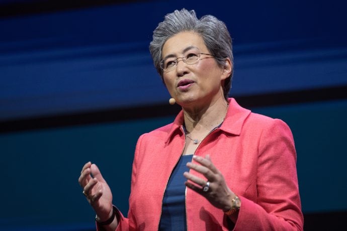 Eine Frau (Lisa Su) mit kurzen grauen Haaren, die eine Brille und einen korallenroten Blazer trägt, spricht auf der Bühne mit einem Kopfbügelmikrofon über AMD und gestikuliert mit den Händen.