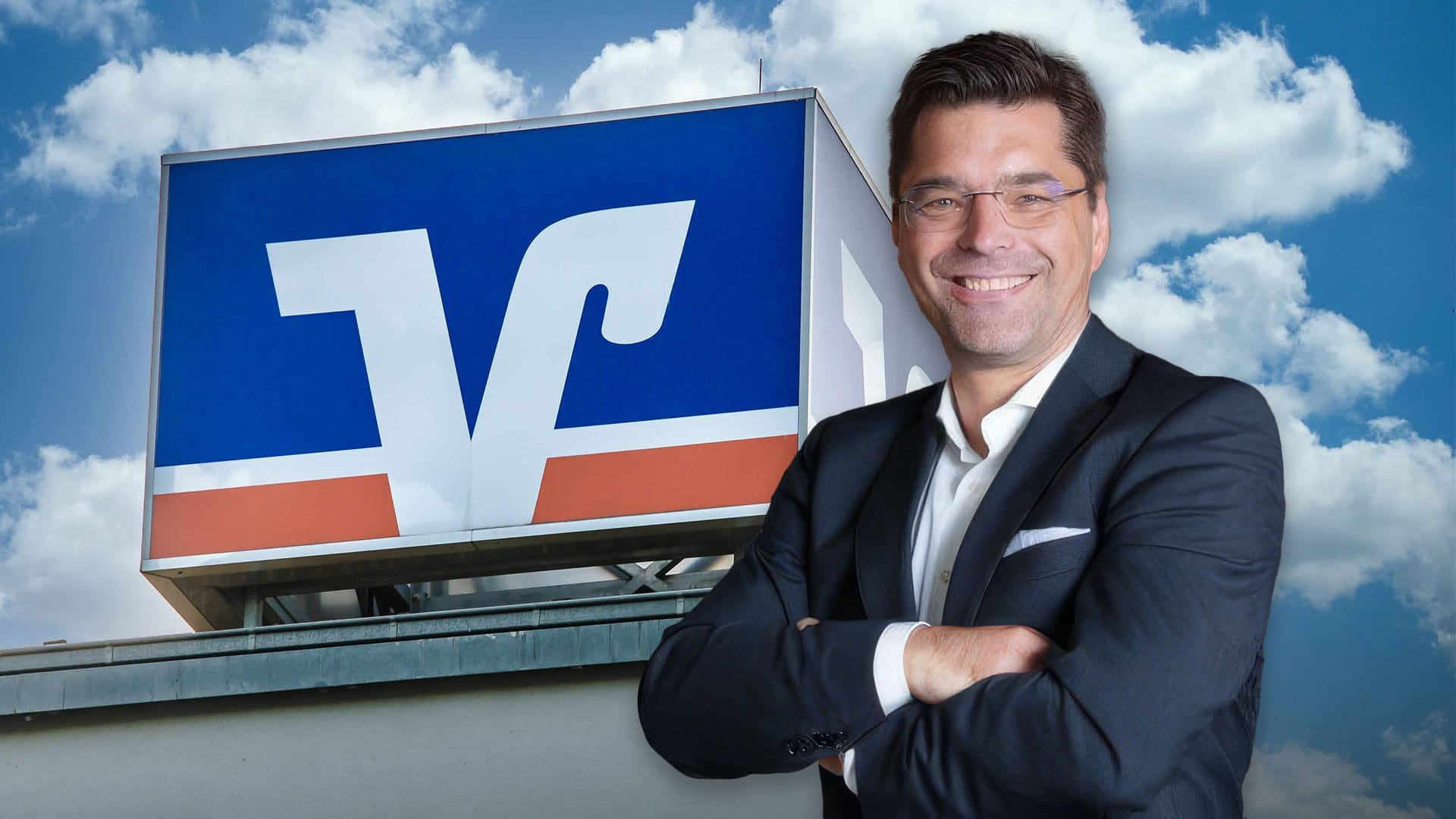 Ein Mann in einem schwarzen Anzug steht lächelnd mit verschränkten Armen vor einem Gebäude mit einem blau-weiß-orangen Bitcoin-Logo.