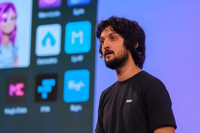 Armani Ferrante spricht über Backpack und Solana Ein Mann mit einem Headset-Mikrofon steht vor einem Bildschirm, auf dem App-Symbole, Grafiken und Krypto-Logos angezeigt werden, und hält eine Präsentation.