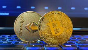 Zwei physische Münzen, die Ethereum und Bitcoin darstellen, stehen auf einer beleuchteten Tastatur, während im Hintergrund auf einem Laptopbildschirm ein Bitcoin-Kurschart mit Allzeithoch aus der aktuellen Handelswoche zu sehen ist.