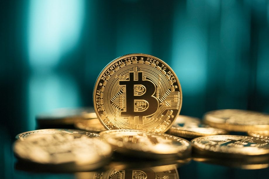 Eine Nahaufnahme von mehreren goldfarbenen Bitcoin-Münzen mit dem ikonischen Symbol vor einem unscharfen blauen Hintergrund.