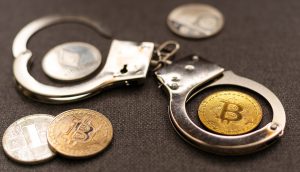 Ein Paar Metallhandschellen und mehrere Kryptowährungsmünzen, darunter Bitcoin und Ethereum, sind auf einer dunklen Fläche ausgestellt und verdeutlichen die Komplexität von Sicherheit und Regulierung im Zusammenhang mit Bitcoin.