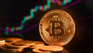 Im Vordergrund ist ein Stapel Bitcoin-Münzen zu sehen, während im unscharfen Hintergrund ein digitales Finanzdiagramm mit Candlestick- und Liniendiagrammen zu sehen ist, die die neuesten Bitcoin-Kurs-Trends veranschaulichen.