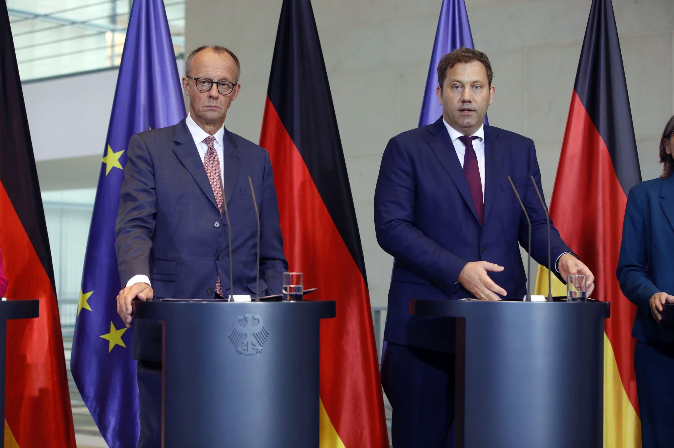 Zwei deutsche Politiker bei einer Pressekonferenz, umgeben von EU- und Deutschlandfahnen – im Kontext wachsender Kritik aus der Bitcoin-Szene am politischen System.