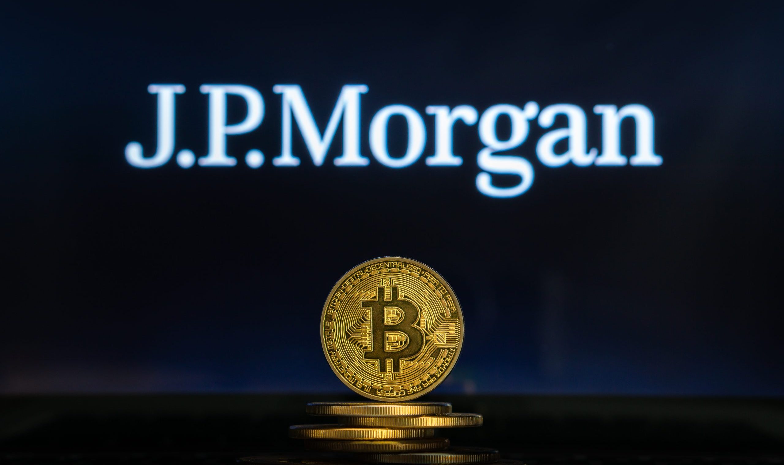 Eine goldene Bitcoin-Münze ist vor anderen Münzen gestapelt, hinter denen das JPMorgan-Logo und das Kursziel auf einem dunklen Hintergrund zu sehen sind.