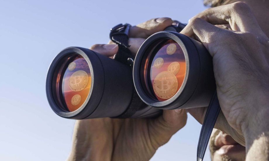 Eine Person, die durch ein Fernglas schaut, in dessen Linsen sich Bitcoin-Symbole vor einem klaren Himmel spiegeln, was auf die Suche nach Bitcoin-Möglichkeiten hinweist.