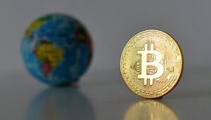 Eine physische Bitcoin-Münze steht aufrecht auf einer spiegelnden Oberfläche, die Bitcoin-Reserven symbolisiert, mit einer kleinen verschwommenen Weltkugel im Hintergrund.