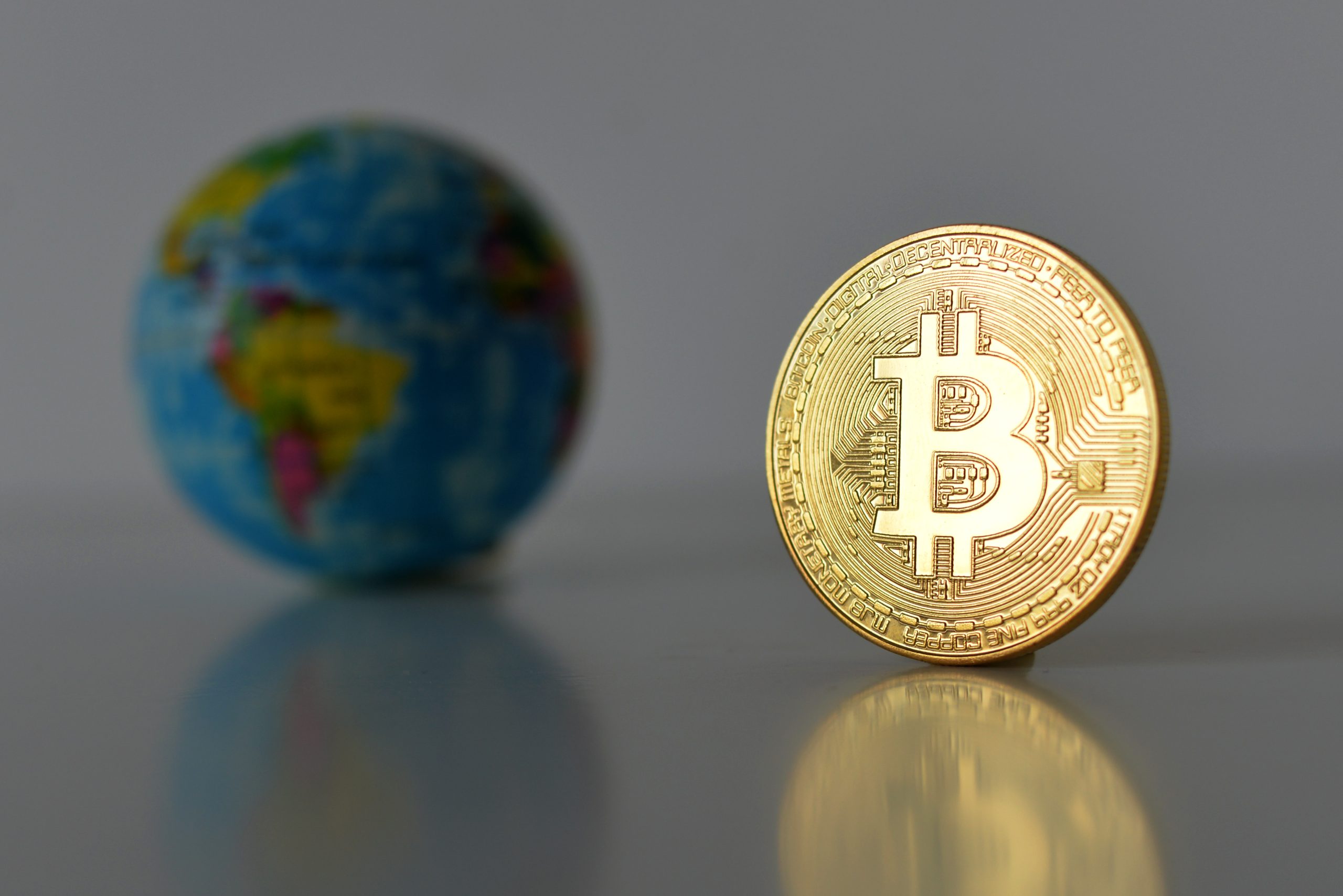 Eine physische Bitcoin-Münze steht aufrecht auf einer spiegelnden Oberfläche, die Bitcoin-Reserven symbolisiert, mit einer kleinen verschwommenen Weltkugel im Hintergrund.