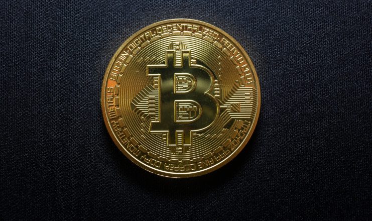 Eine goldfarbene Bitcoin-Münze mit dem Bitcoin-Symbol ruht auf einem schwarzen, strukturierten Hintergrund.