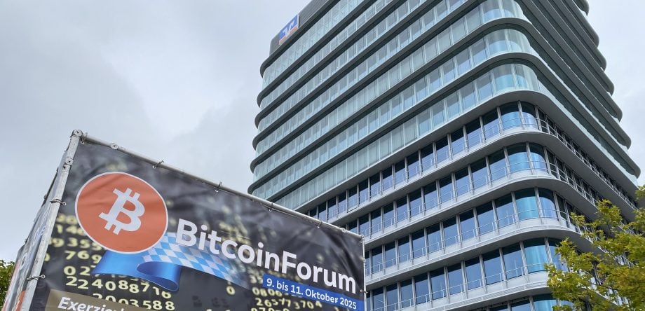 Ein BitcoinForum-Banner mit dem Bitcoin-Logo steht vor einem modernen gläsernen Bürogebäude unter einem bewölkten Himmel.