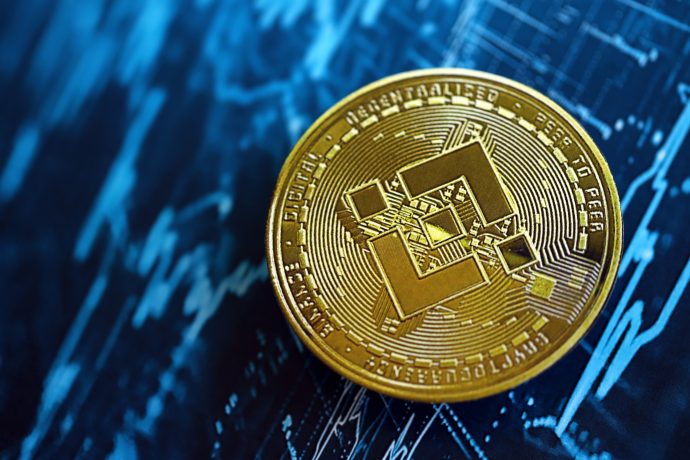 Eine goldene BNB Binance-Münze ruht auf einem blauen Hintergrund, auf dem Finanzcharts und Datengrafiken zu sehen sind.