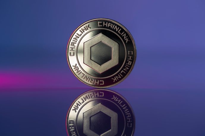Eine Chainlink-Kryptowährungsmünze steht aufrecht auf einer reflektierenden Oberfläche und zeigt das Chainlink-Logo vor einem auffälligen Hintergrund mit lila und blauem Farbverlauf.