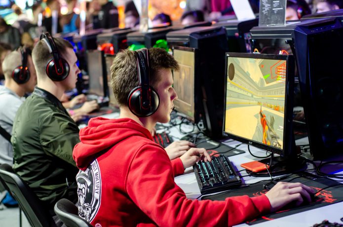 Mehrere junge Leute mit Headsets sitzen an Computern und spielen CS2, ein Ego-Shooter-Videospiel, bei einem esports-Event oder Gaming-Turnier.
