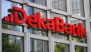 Rotes DekaBank-Schild an der Glasfassade eines modernen Gebäudes, mit Spiegelungen anderer Gebäude und Bäume, die die Boerse Stuttgart Digital und die DekaBank hervorheben: Ausbau der Partnerschaft beim Krypto-Handel.