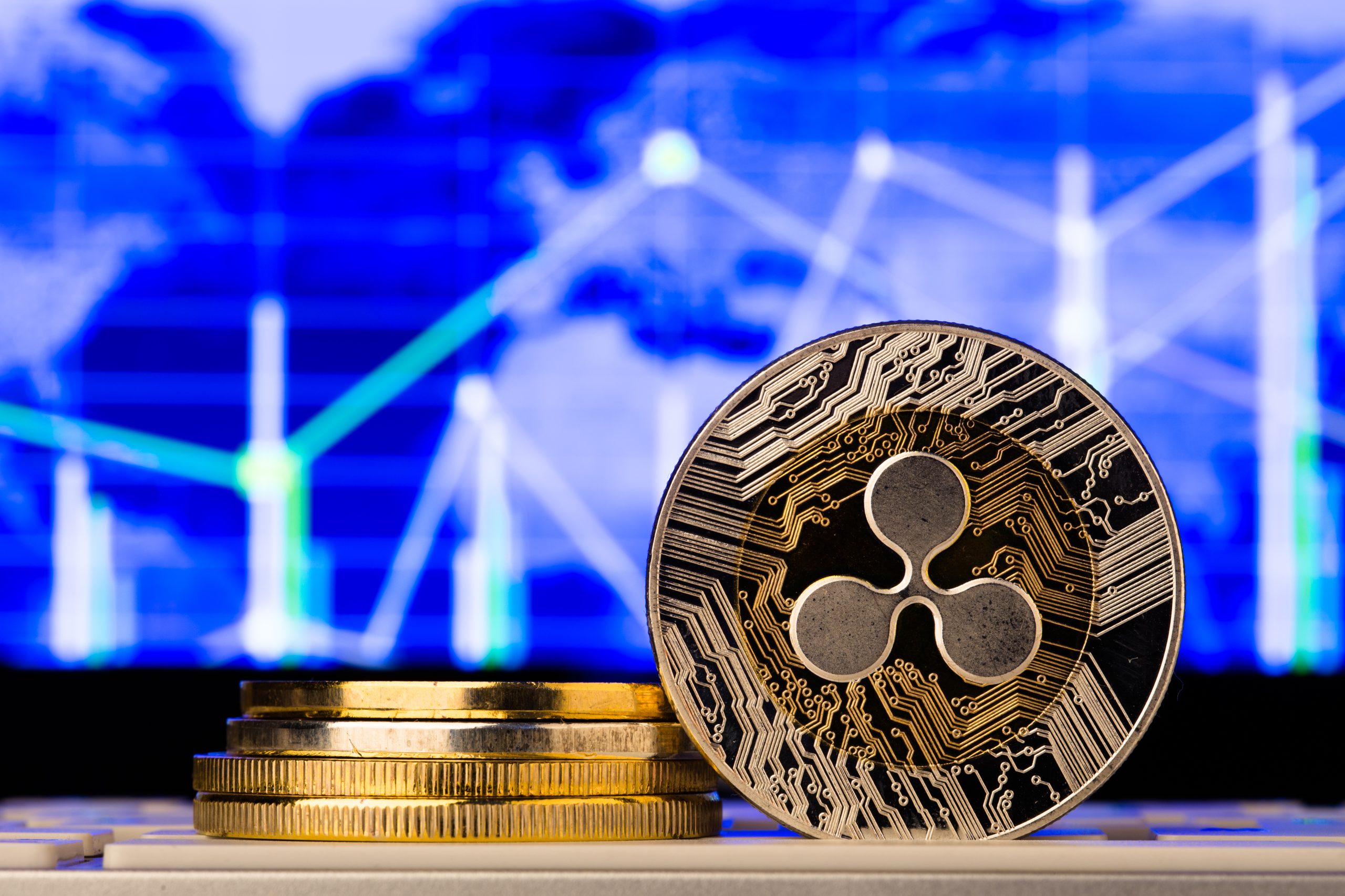 Ein Stapel Goldmünzen und eine Münze der Kryptowährung XRP werden vor einer blauen digitalen Weltkarte mit Finanzgrafiken angezeigt.