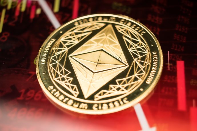Ein goldener Ethereum Classic Coin ruht auf einem Hintergrund, der rote Finanzgraphen und Börsendaten anzeigt, was auf eine potenzielle Kaufgelegenheit während des jüngsten Krypto-Crashs hindeutet.