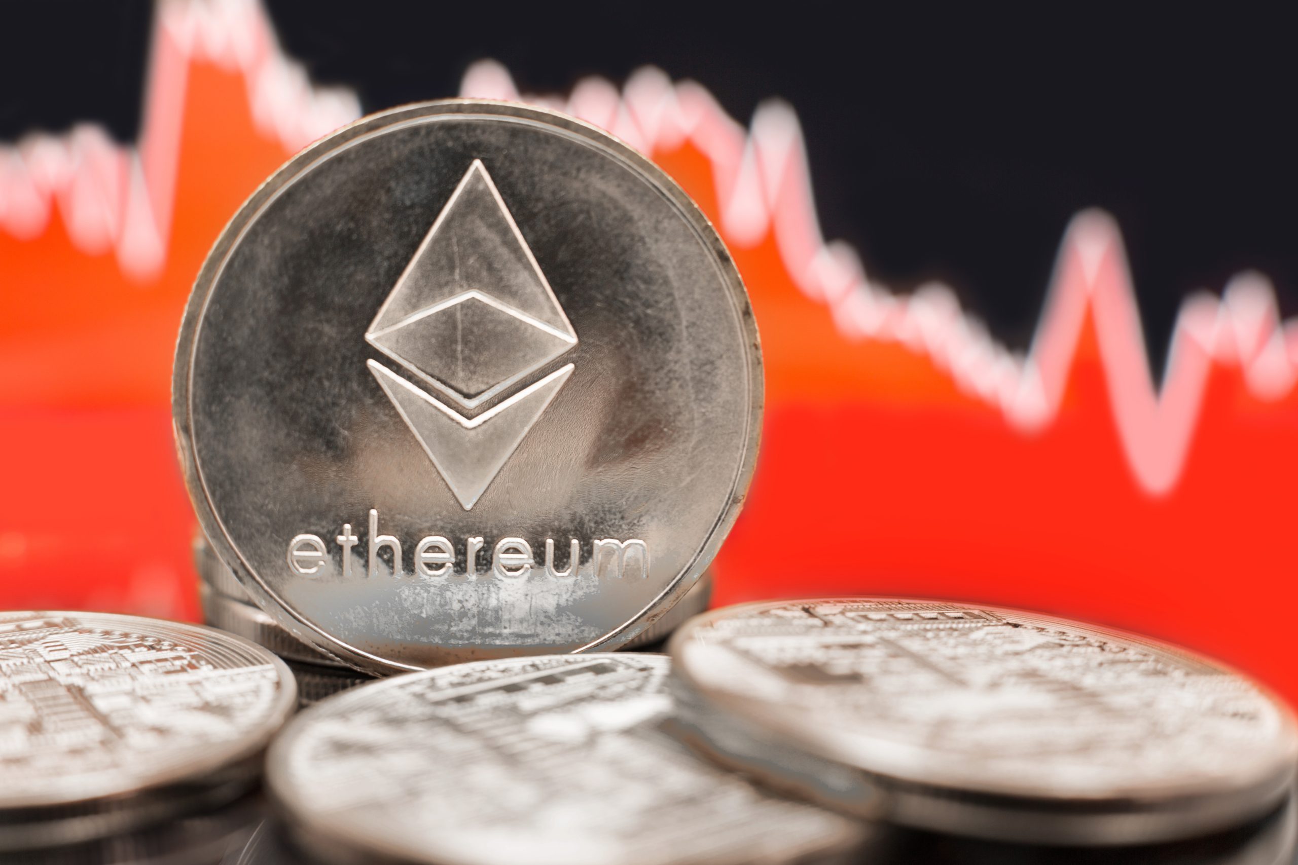 Droht nach dem Treasury-Hype der Ethereum-Crash? Nahaufnahme von ETH-Münzen mit einem roten, rückläufigen Aktienchart im Hintergrund, der auf einen Wertverlust der Kryptowährung hindeutet.