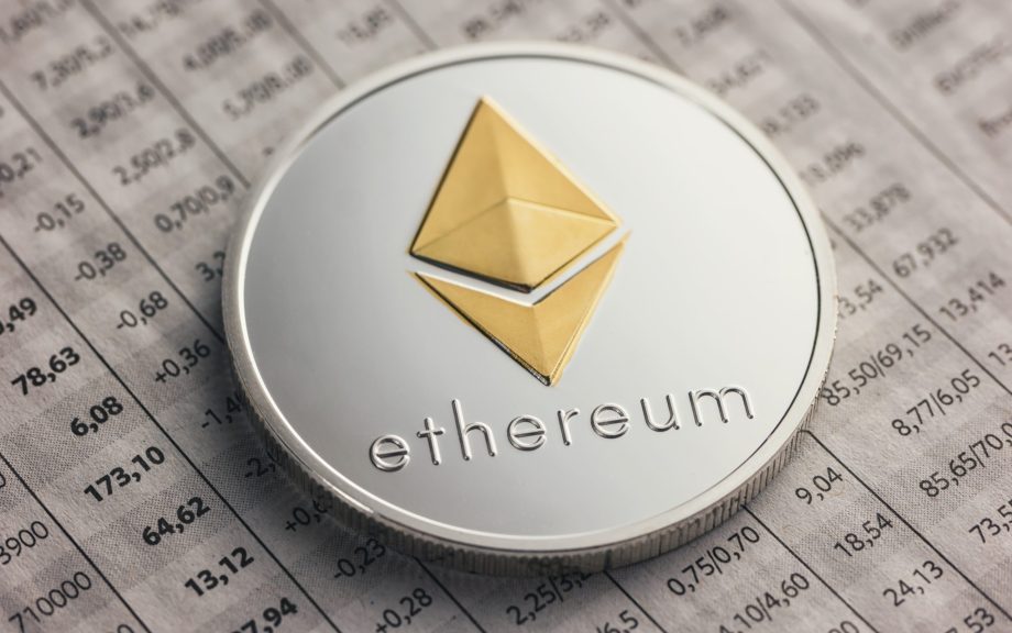 Eine silberne Ethereum-Münze mit einem goldenen Logo ruht auf einem gedruckten Arbeitsblatt, auf dem numerische Finanzdaten zur Leistung von Ethereum stehen.
