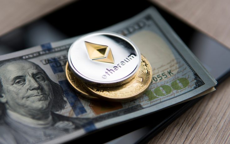 ethereum-treasury-bitmine-14-milliarden-usd Eine silberne Ethereum-Münze und zwei Goldmünzen liegen auf einem 100-US-Dollar-Schein, der auf einem schwarzen Smartphone auf einer hölzernen Oberfläche platziert ist - ein Symbol für digitale Vermögenswerte wie BitMine in der modernen Finanzlandschaft.