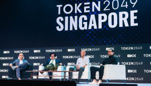 Vier Männer, darunter Sam Tabar, sitzen während einer Podiumsdiskussion auf der TOKEN2049-Veranstaltung in Singapur auf einer Bühne, während im Hintergrund das Branding der Veranstaltung und Gespräche über Bitcoin zu sehen sind.