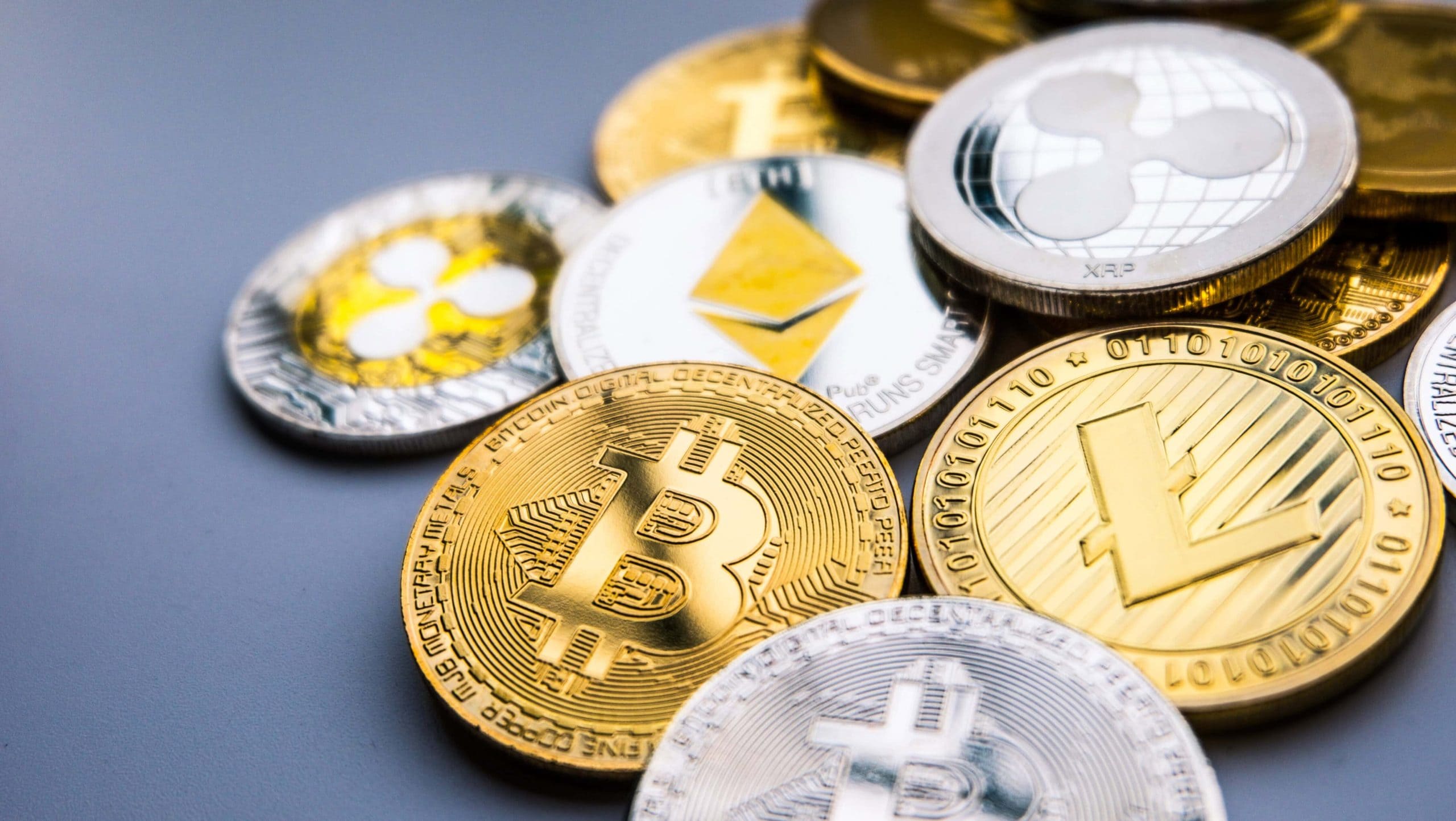 Verschiedene physische Münzen, die verschiedene Kryptowährungen repräsentieren, darunter Bitcoin, Ethereum, Ripple, Litecoin und andere beliebte Altcoins, die auf einer grauen Oberfläche angezeigt werden.