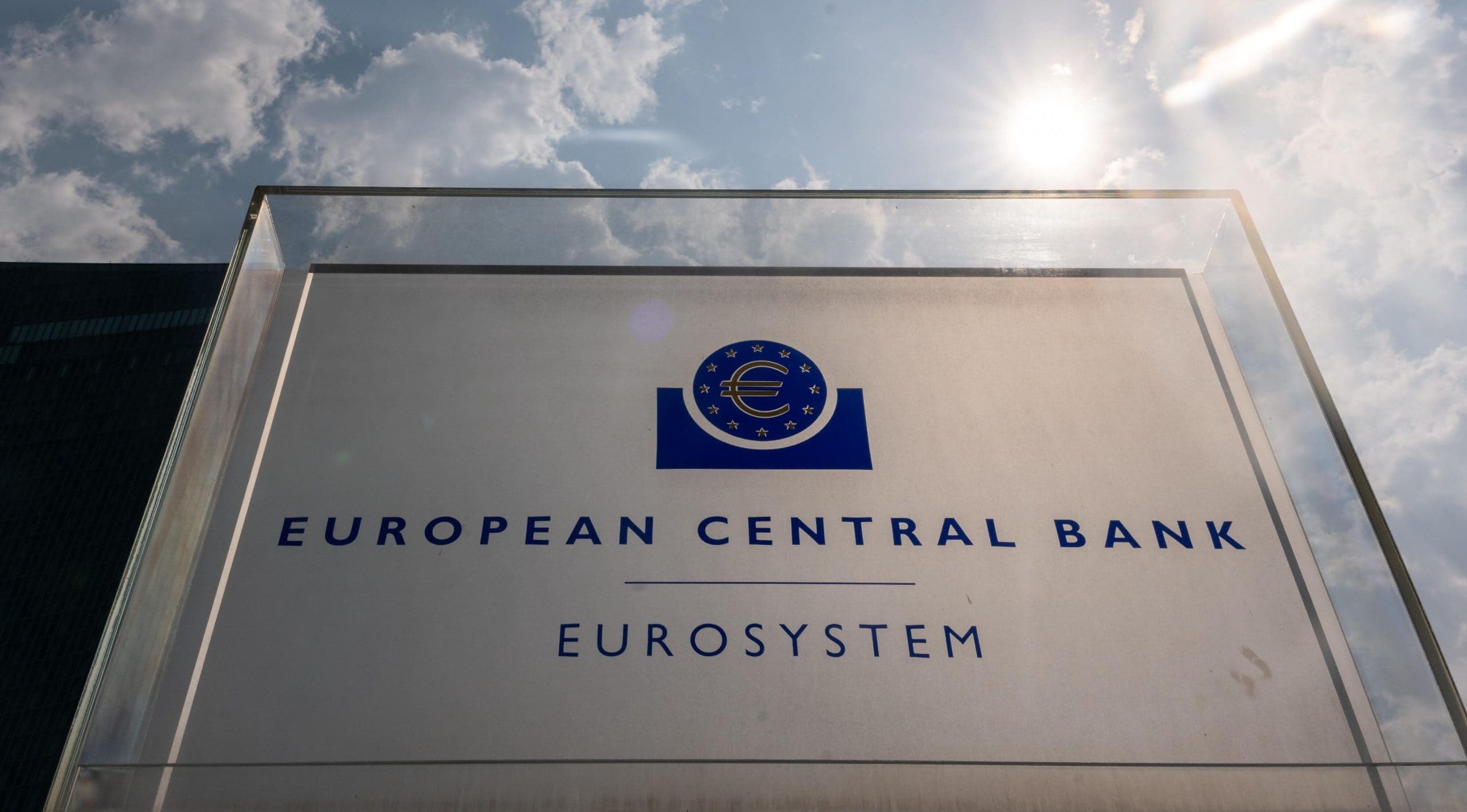 Der digitale Euro wird von der Europäischen Zentralbank ausgegeben werden Schild für die Europäische Zentralbank mit dem Logo und dem Wort Eurosystem, fotografiert im Freien bei teilweise bewölktem Himmel mit Sonnenlicht im Hintergrund.