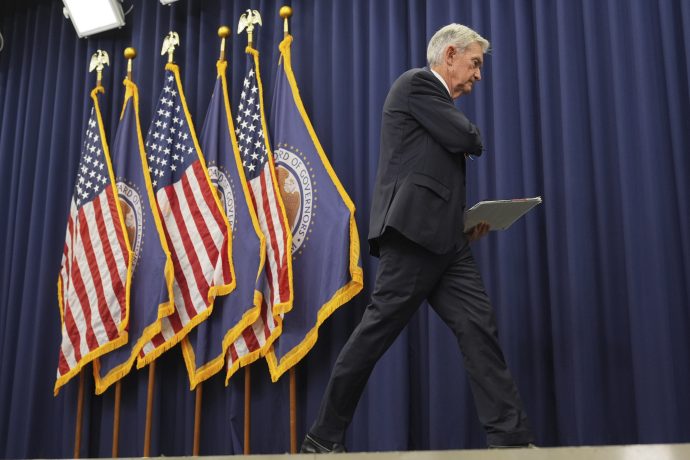 fed-chef-5-kandidaten Ein Mann im Anzug geht über die Bühne und hält eine Mappe in der Hand. Im Hintergrund sind mehrere Flaggen der USA und der Federal Reserve zu sehen - möglicherweise einer von Powells Nachfolge-Kandidaten.