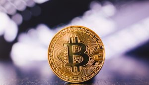 Ein goldfarbener Bitcoin mit dem ikonischen Bitcoin-Logo steht aufrecht auf einer spiegelnden Oberfläche mit einem unscharfen Hintergrund.