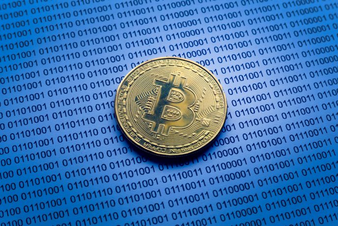 GM3 tokenisiert Unternehmensanteile direkt auf der Bitcoin-Blockchain Eine goldfarbene Bitcoin-Münze ruht auf einer Oberfläche, die mit Reihen von Binärcodes bedeckt ist und die digitale Grundlage von Bitcoin hervorhebt.
