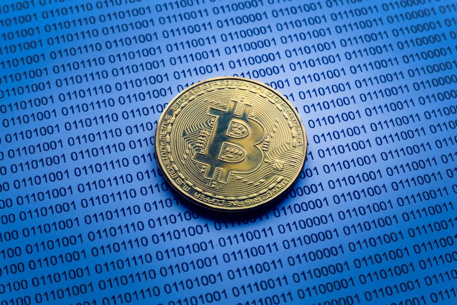 Eine goldfarbene Bitcoin-Münze ruht auf einer Oberfläche, die mit Reihen von Binärcodes bedeckt ist und die digitale Grundlage von Bitcoin hervorhebt.