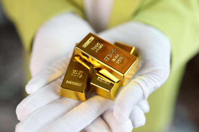 Goldpreis-Absturz verunsichert Anleger – ist die Rallye schon vorbei? Eine Person mit weißen Handschuhen hält mehrere glänzende Goldbarren in der Hand, deren polierte Oberflächen das Licht reflektieren und auf denen komplizierte Goldgravuren zu sehen sind.
