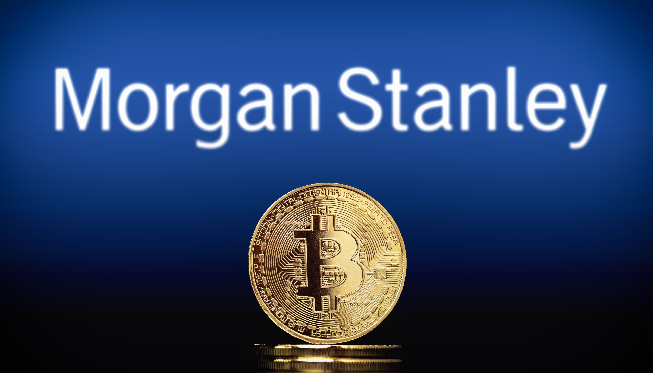 Eine physische Bitcoin-Münze steht vor einem unscharfen Morgan-Stanley-Logo, das die Überschneidung von traditionellem Finanzwesen und digitalen Vermögenswerten verdeutlicht.
