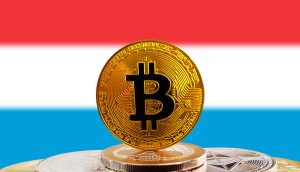 Mehrere Kryptowährungsmünzen, darunter Bitcoin, werden vor dem Hintergrund einer luxemburgischen Flagge gezeigt.