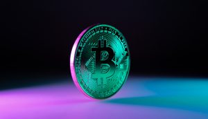 Der Krypto-Markt wartet auf Impulse Eine physische Bitcoin-Münze steht aufrecht auf einer Fläche, die von blauem und violettem Licht beleuchtet wird, vor einem dunklen Hintergrund mit Farbverlauf, auf dem das ikonische Bitcoin-Symbol zu sehen ist.