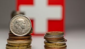 Stapel von Frankenmünzen sind vor einer Schweizer Flagge angeordnet, die ein weißes Kreuz auf rotem Grund zeigt – ein Symbolbild für den Frankencoin.
