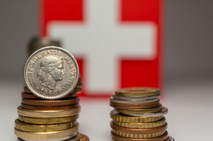 Stapel von Frankenmünzen sind vor einer Schweizer Flagge angeordnet, die ein weißes Kreuz auf rotem Grund zeigt – ein Symbolbild für den Frankencoin.