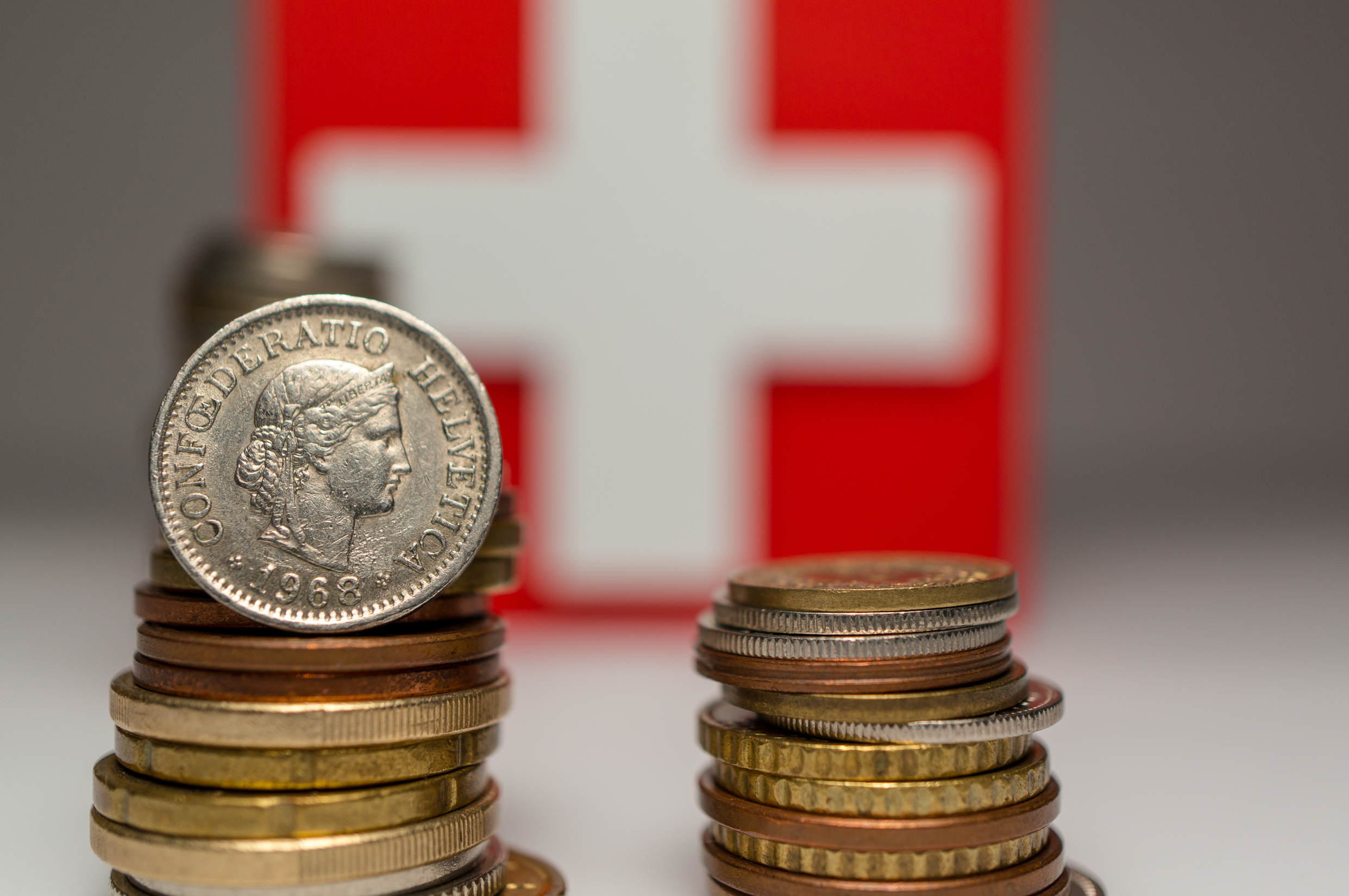 Stapel von Frankenmünzen sind vor einer Schweizer Flagge angeordnet, die ein weißes Kreuz auf rotem Grund zeigt – ein Symbolbild für den Frankencoin.