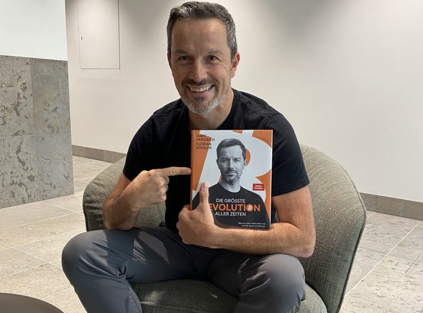 Der Finanzexperte Marc Friedrich präsentiert im Interview seinen aktuellen Bestseller „Die größte Revolution aller Zeiten“. In entspannter Atmosphäre, gekleidet in sportlich-bunten Sneakern, sitzt er auf einem Lounge-Sessel und hält das Buch mit einem breiten Lächeln in die Kamera. Das Cover zeigt ein Porträt von Friedrich – thematisch dreht sich das Werk um Systemwandel, wirtschaftliche Disruption und die Rolle von Bitcoin im Umbruch der Finanzwelt.