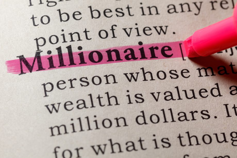 Nahaufnahme einer Wörterbuchseite, auf der das Wort Millionär rosa hervorgehoben und teilweise mit einem rosa Marker unterstrichen ist - eine subtile Anspielung auf die moderne Paper-Millionäre.