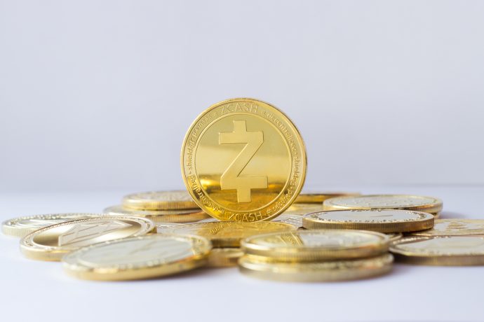 Zcash,Coin,Stand,On,Other,Cryptocurrencies.,Pale,Blue,Background. Eine Gruppe goldfarbener Zcash-Münzen ist gestapelt und ausgebreitet, wobei eine Münze aufrecht in der Mitte steht und das Engagement von Zcash für die Privatsphäre vor einem schlichten weißen Hintergrund symbolisiert.