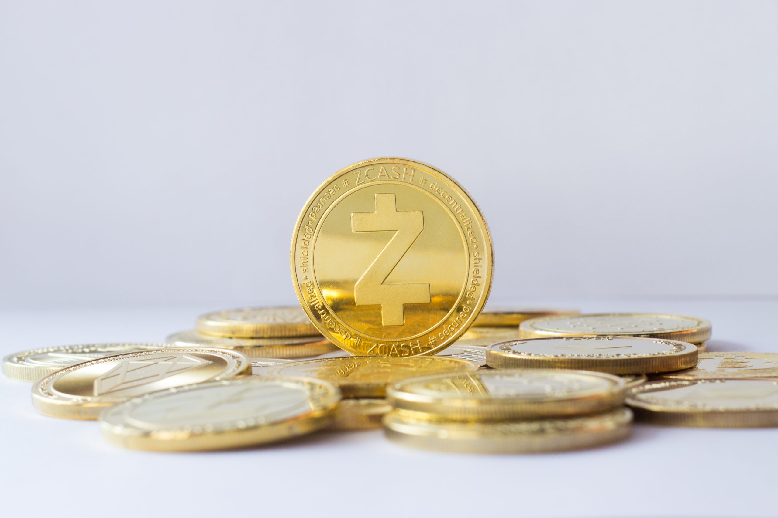 Zcash,Coin,Stand,On,Other,Cryptocurrencies.,Pale,Blue,Background. Eine Gruppe goldfarbener Zcash-Münzen ist gestapelt und ausgebreitet, wobei eine Münze aufrecht in der Mitte steht und das Engagement von Zcash für die Privatsphäre vor einem schlichten weißen Hintergrund symbolisiert.