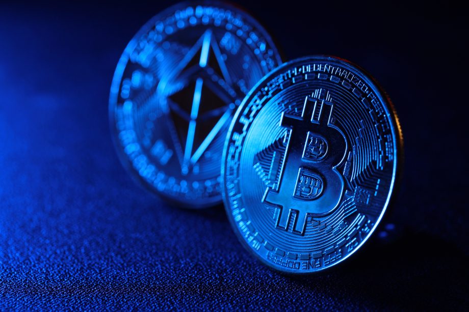 Nahaufnahme von zwei physischen Kryptowährungsmünzen, eine mit einem Bitcoin-Symbol und die andere mit einem Ethereum-Symbol, beleuchtet mit blauem Licht - perfekt für alle, die sich für den Krypto-Markt interessieren.