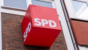 An der Außenseite eines Backsteingebäudes ist unter zwei Fenstern ein rotes Würfelschild mit fetten weißen SPD-Schriftzügen angebracht.