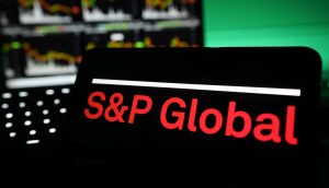 Auf einem Bildschirm wird das Logo von S&P Global in roter Schrift angezeigt, während im Hintergrund unscharfe S&P-Finanzcharts und -Grafiken zu sehen sind.