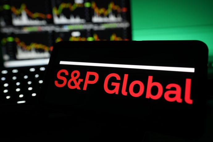 Auf einem Bildschirm wird das Logo von S&P Global in roter Schrift angezeigt, während im Hintergrund unscharfe S&P-Finanzcharts und -Grafiken zu sehen sind.