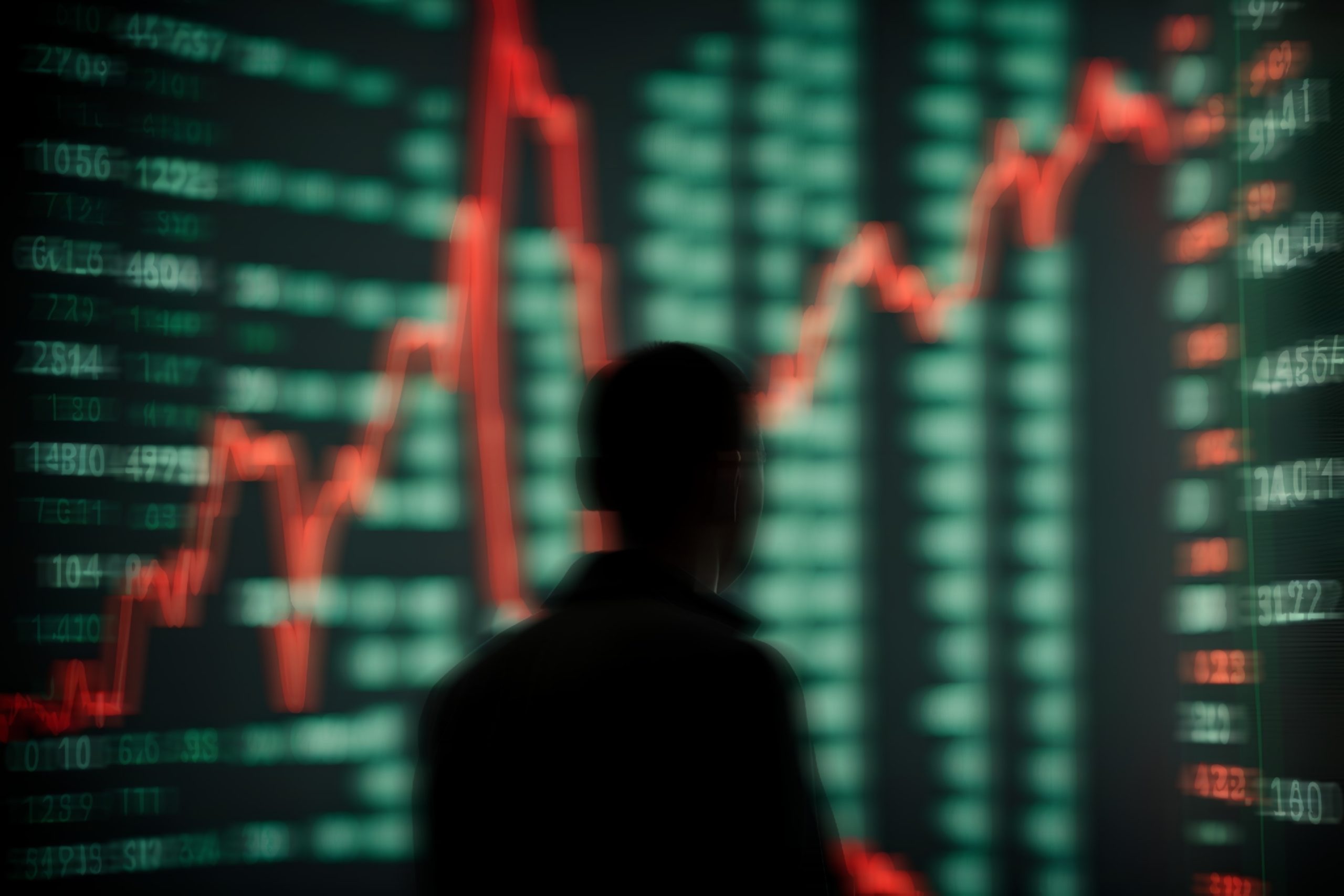 Eine Person steht vor einem großen digitalen Display, das schwankende Aktiencharts, Finanzdaten und Stripe-Zahlungsanalysen in Rot und Grün anzeigt.