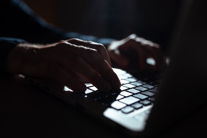 Nahaufnahme von Händen, die bei schwachem Licht auf einer Laptop-Tastatur tippen, während die Telegram-App auf dem Bildschirm geöffnet ist.