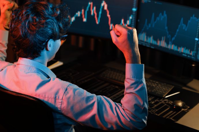 Trader mit erhobener Faust vor mehreren Monitoren mit fallenden Krypto-Kursen – Symbolbild für Marktvolatilität und Liquidationen.